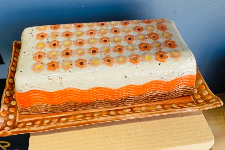 Decorative ceramic cake with orange layers and floral top on a patterned platter.