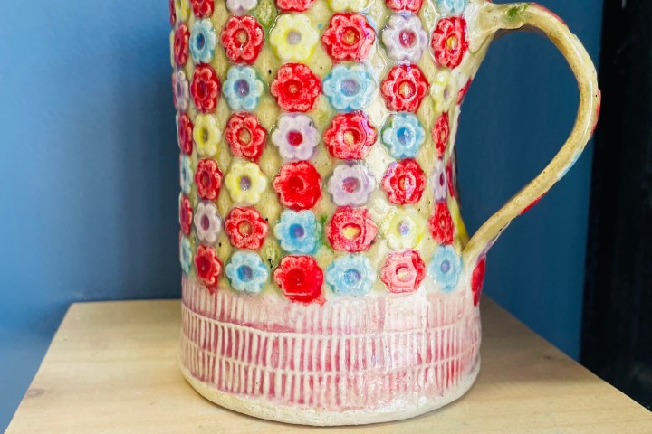 Colorful floral-patterned ceramic mug on wooden shelf with a blue wall background.