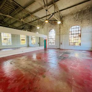Spacious room with red floor, large windows, mirrors, and exposed beams.