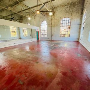 Empty industrial loft space with red concrete floor and large windows.