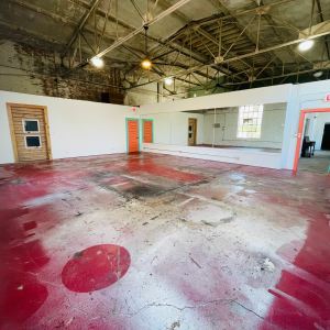 Spacious industrial room with red floor, high ceiling, and mirrors on one wall.