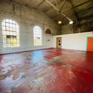 Spacious empty room with red floor, large windows, and colorful doors.