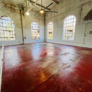 Spacious industrial room with red floor, tall arched windows, and exposed ceiling beams.