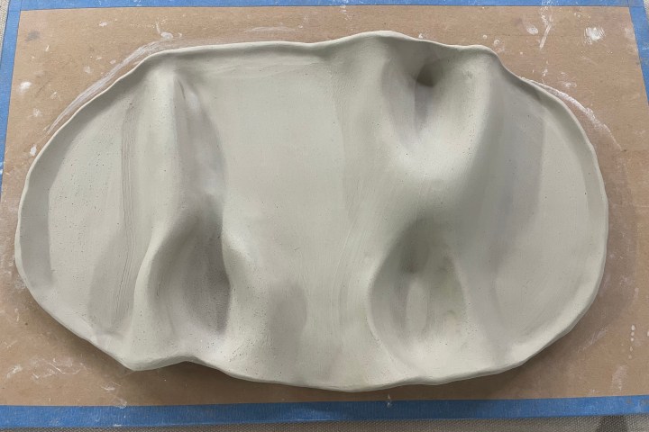 Abstract clay sculpture with wavy, uneven surface on a flat board.