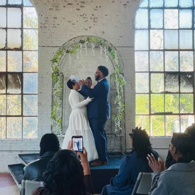 Wedding ceremony with couple under floral arch, guests seated, and person photographing with phone.
