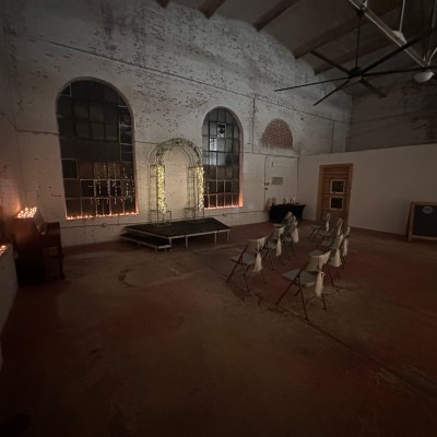 Dimly lit large room with chairs facing a small stage and archway, strings of lights on windows.