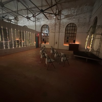 Dimly lit room with chairs, string lights on walls and a small stage.