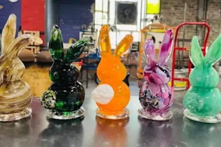 Five colorful glass bunny figurines on a table in a workshop setting.