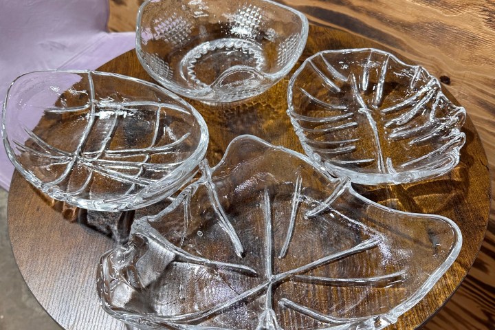 Four glass leaf-shaped bowls on a round wooden table.