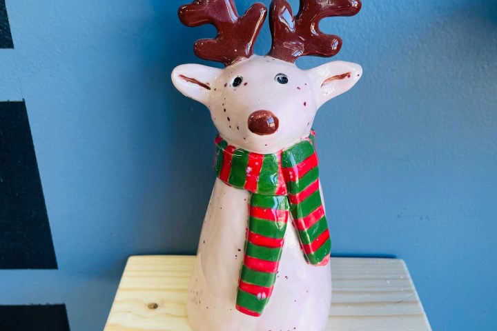 Reindeer figurine with red-green scarf on a wooden shelf.
